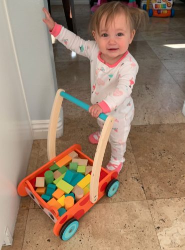 Standing baby holding push cart filled with blocks