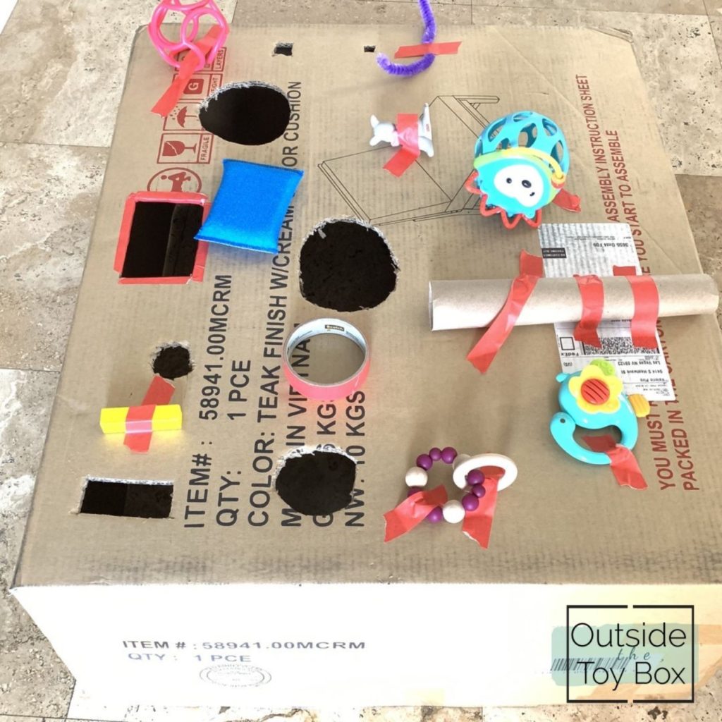 Cardboard box with holes cut out and toys taped on