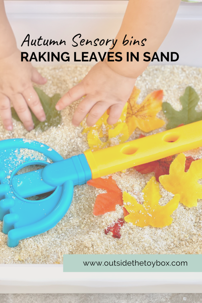 Toddler hands in sand with leaves and rake