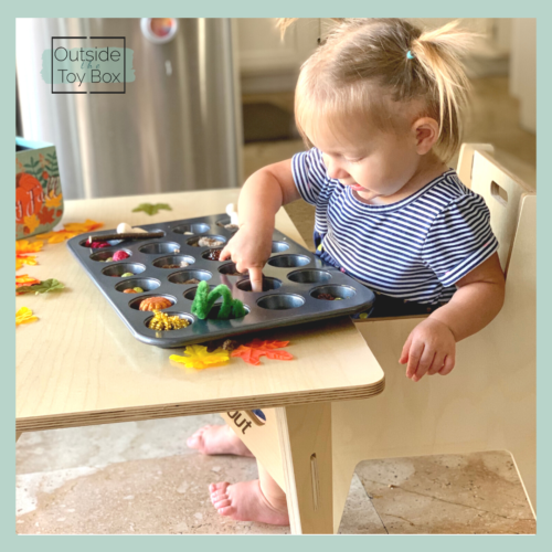 toddler sitting at table playing with play dough in a muffin tin