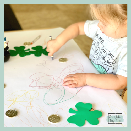 Toddler using crayon to scribble with gold coins and shamrocks
