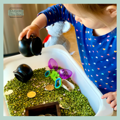 Toddler pouring pot of gold above St. Patrick's Day dry sensory bin