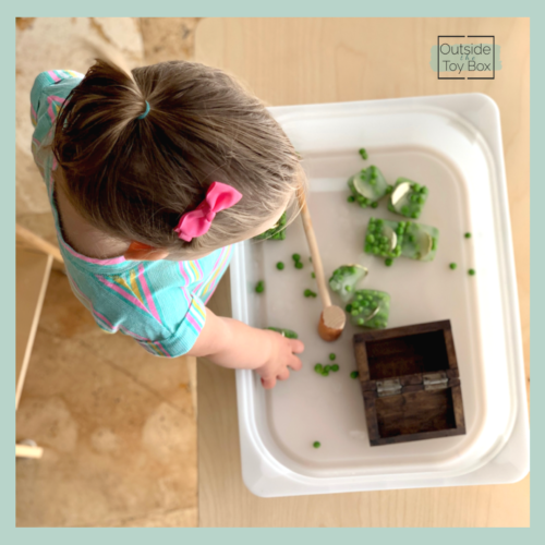 Toddler playing with frozen peas and gold coins sensory bin