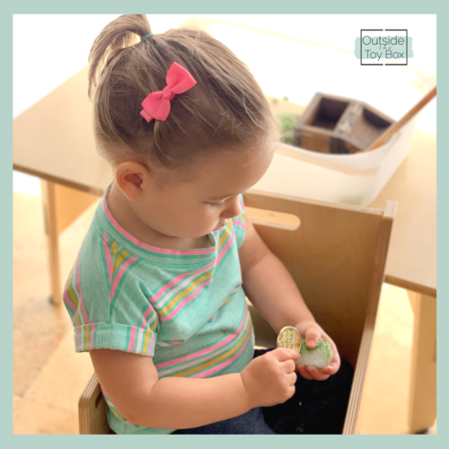 Toddler holding frozen cube of peas and gold coin