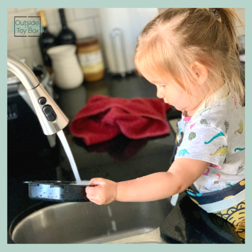 Toddler washing paint tray at the sink