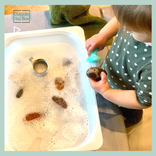 toddler washing rocks with scrubby brush and soapy water