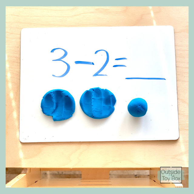 Subtraction problem written on white board with play dough balls