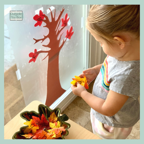 toddler looking at faux fall leaf with letter on it